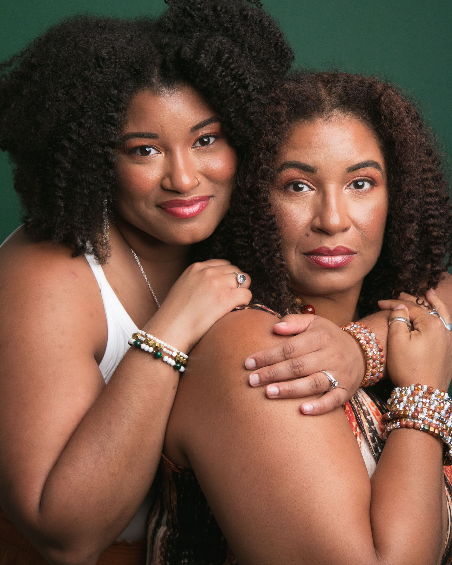 two black women with brown and black curly hair hugging each other soft smiling for camera