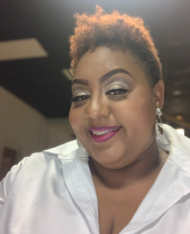 black woman with pixie cut wearing a white polo long sleeve blouse smiling with teeth with bright fuchsia lipstick and silver sparkly eye makeup