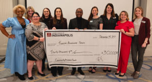 10 people stand in front of a blank wall holding a big check
