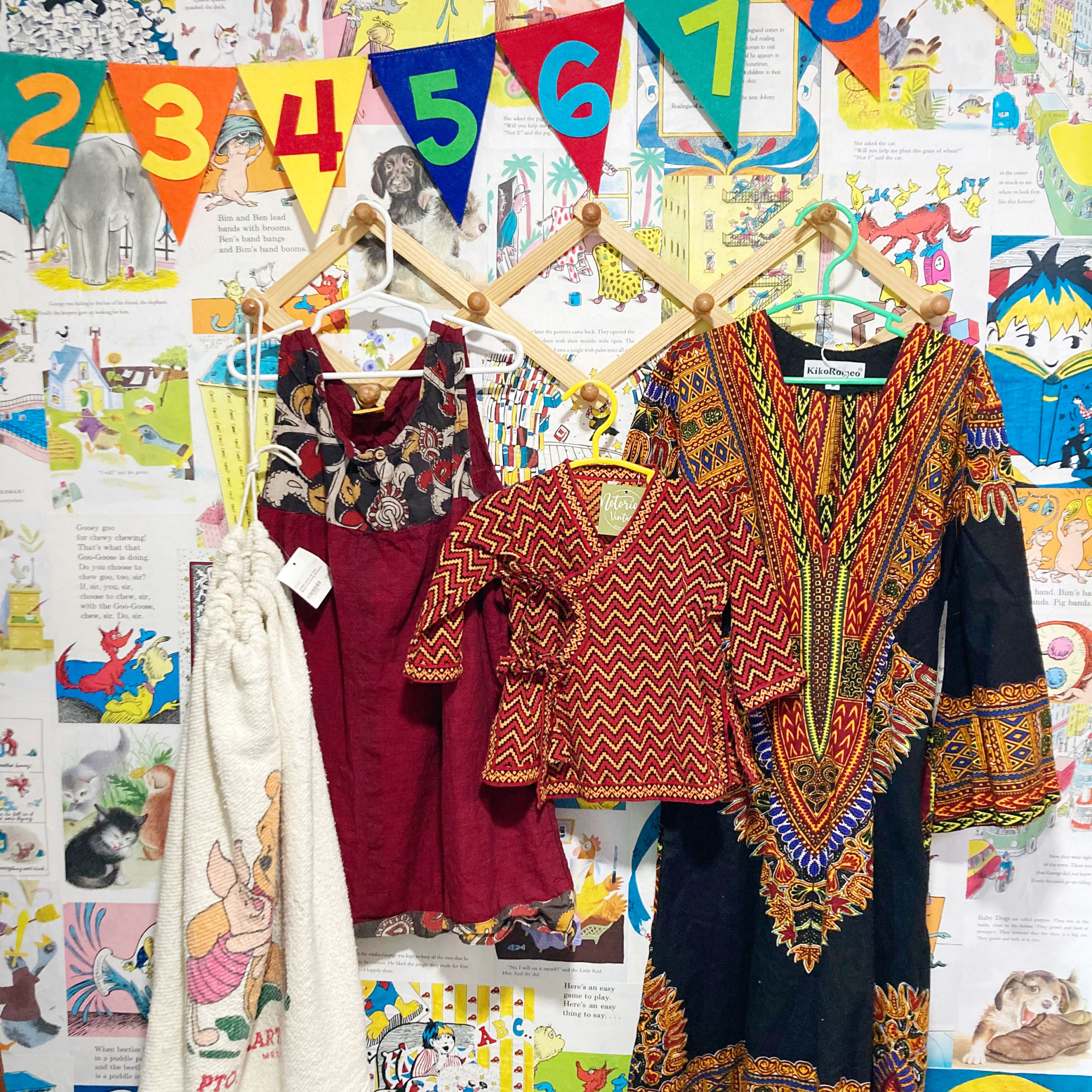 four pieces of clothing with a variety of colorful prints hanging on hangers on a wall with drawings taped onto it