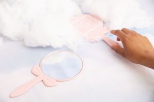 small light pink hand mirror on white background with cloud decorations