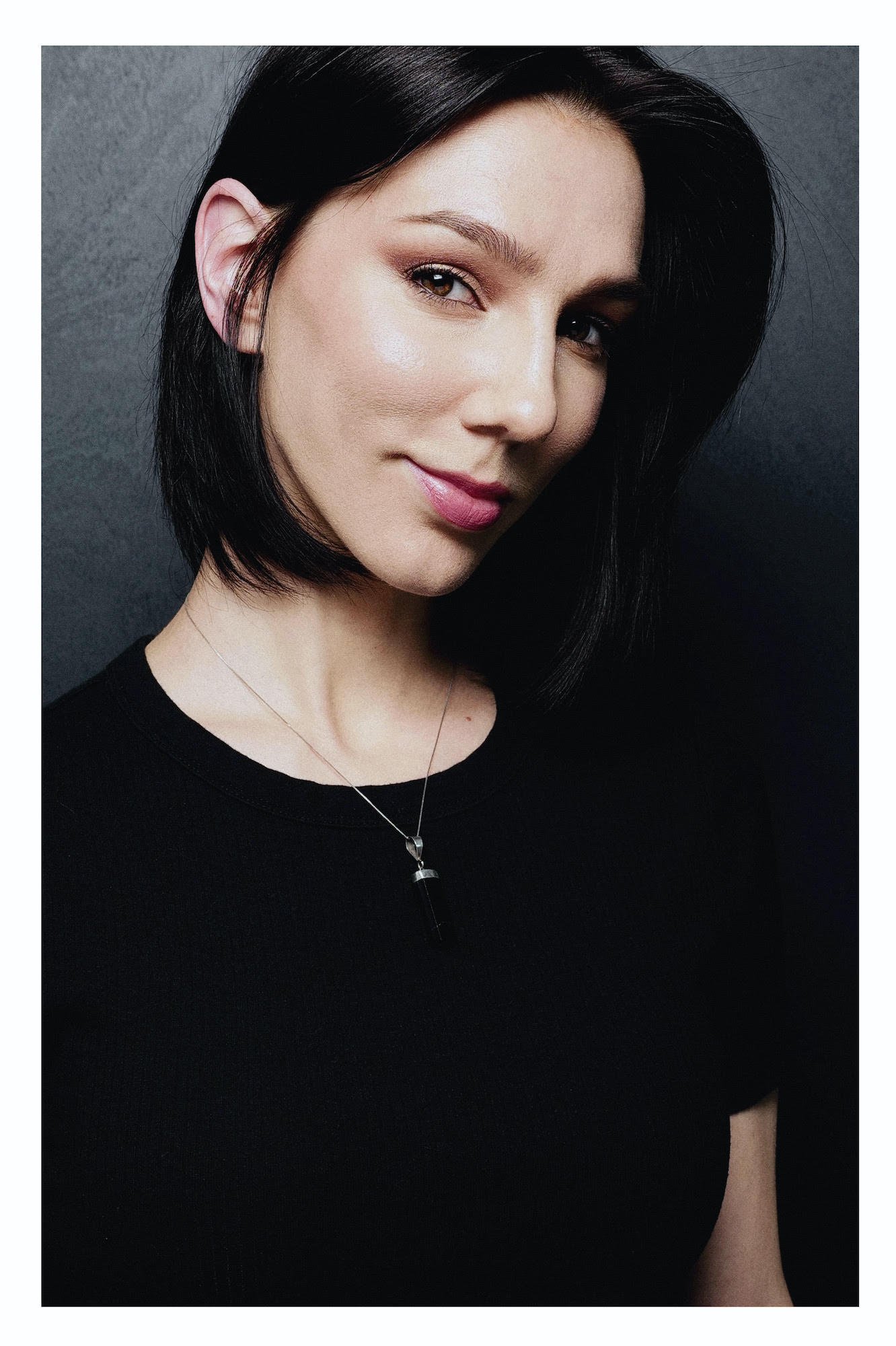 skinny white woman with short black hair wearing black shirt soft smiling for the camera with a side eye