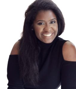 black woman wearing a black sweater exposing her shoulders white long black hair and smiling with teeth for the camera