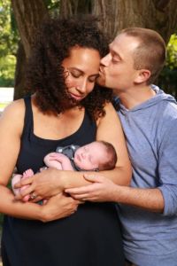 black woman and white man an interracial couple holding a new born baby by a tree