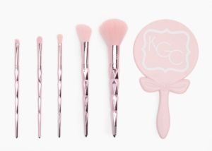 5 pink makeup brushes with a pink mirror on a white background