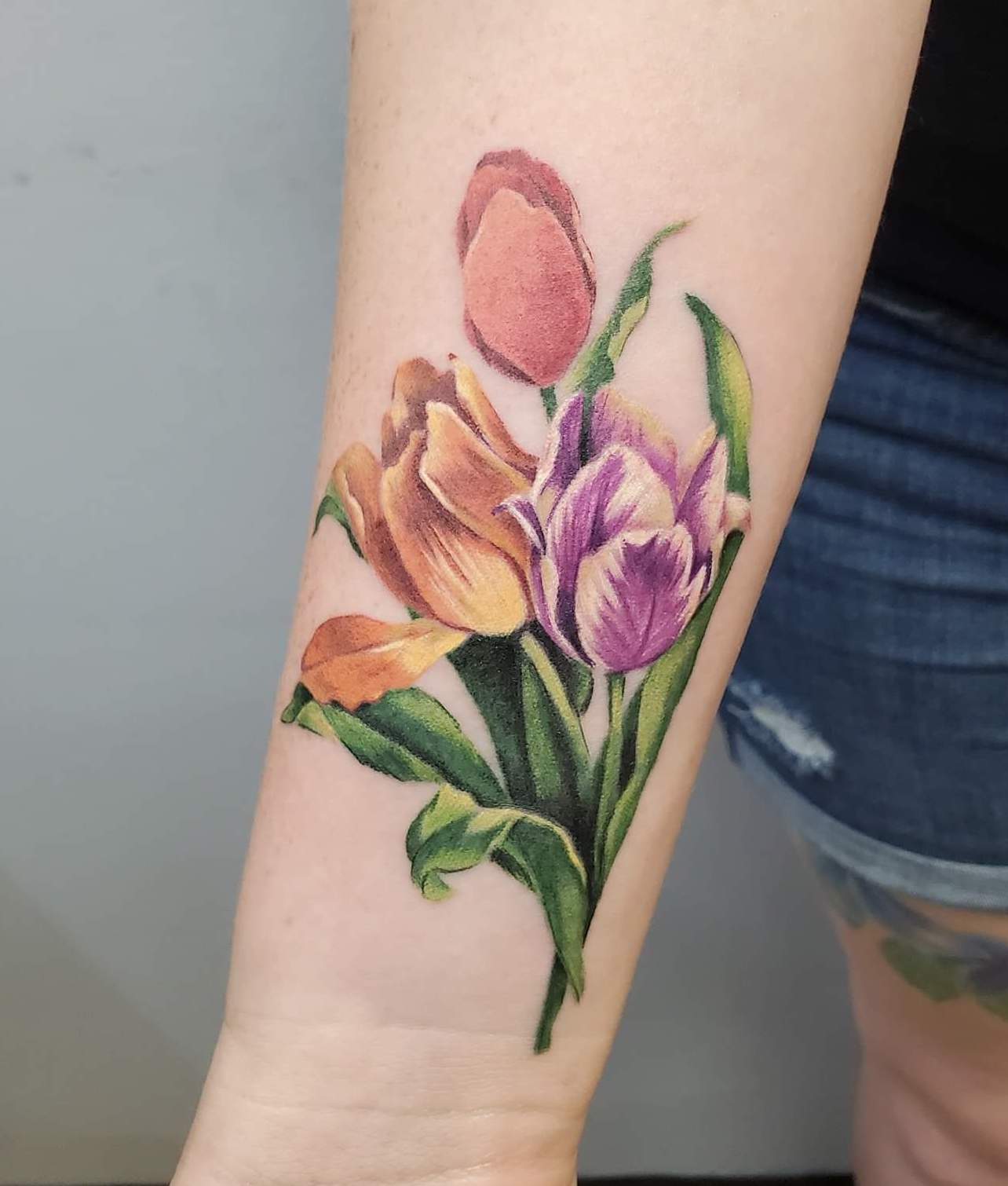 A tattoo of a bouquet of tulips that are purple orange and pink