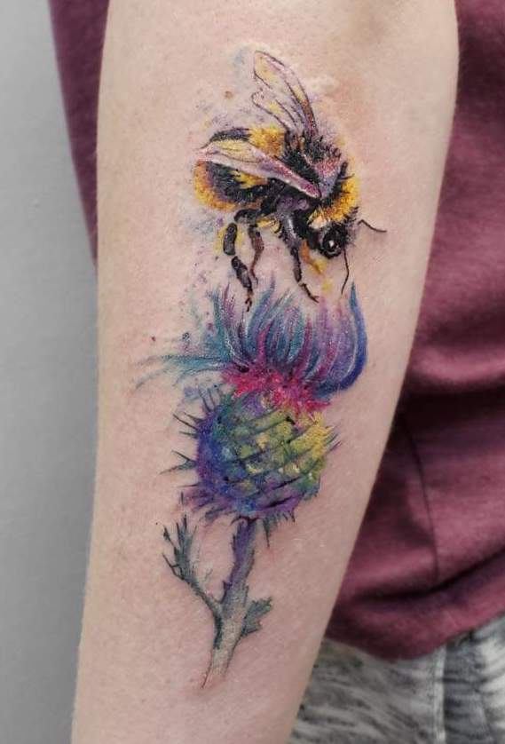a tattoo of a bumblebee flying down to a colorful flower and sucking nectar out