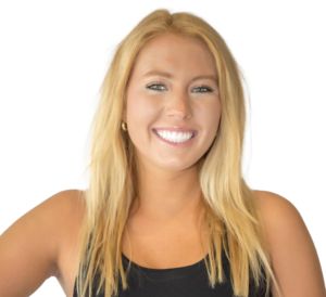 white woman with spray tan and yellowish blonde medium hair smiles with teeth for camera wearing a black tank top