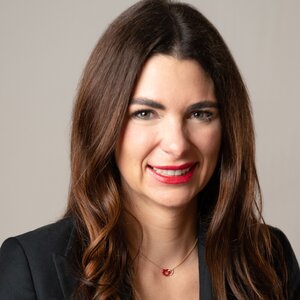 Woman with light brown hair wearing black blazer smiles with teeth wearing red lipstick