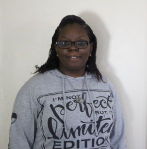 black woman wearing glasses smiling with teeth wearing a grey sweater with black lettering 