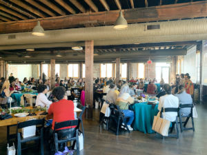 a lot of women sitting at tables in an event space looking forward towards a speaker at a brunch event
