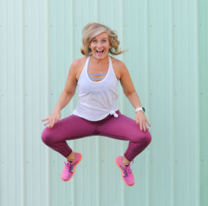 photo of emily nichols in workout clothing jumping in front of a mint green barn