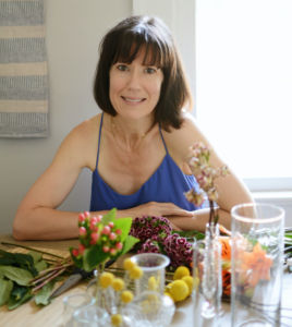 A photo of Maura Malloy smiling in her kitchen wearing a blue tank top