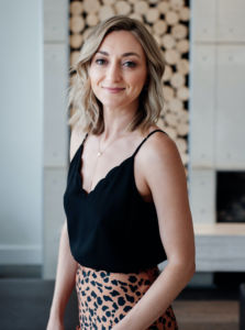a photo of Erin Polley wearing a black tank top and a printed skirt soft smiling