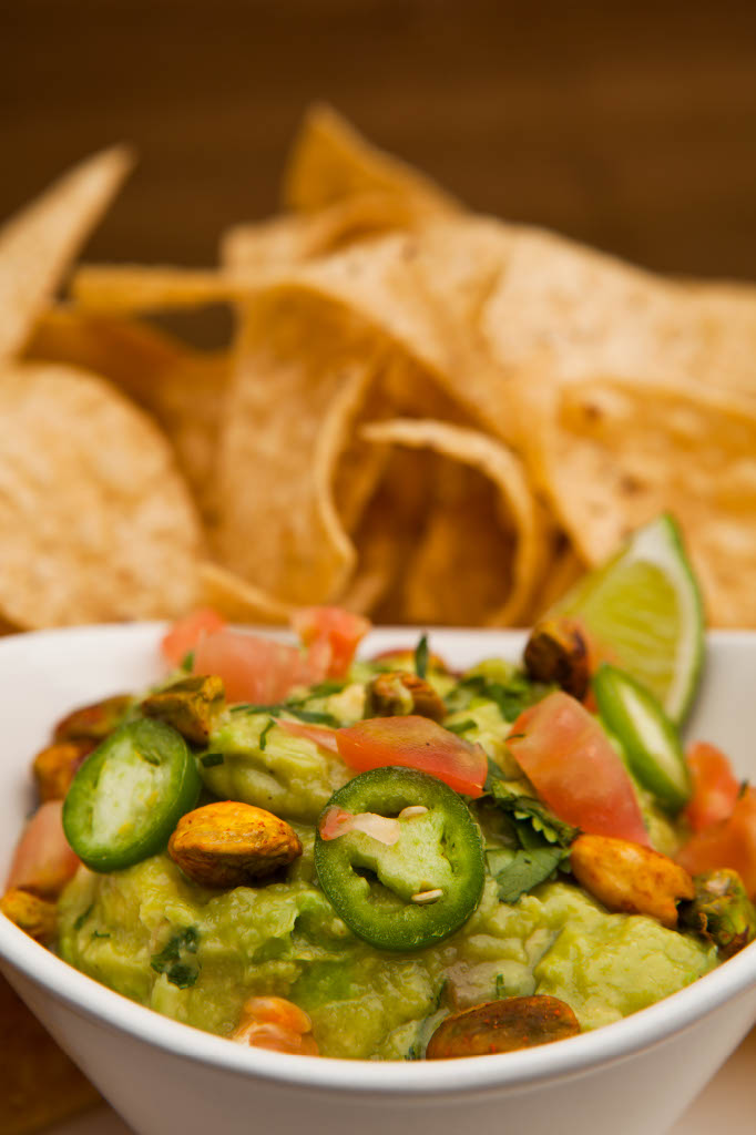 Delicia Guacamole topped with jalapeños, tomatoes, and pistachio with a side of chips.