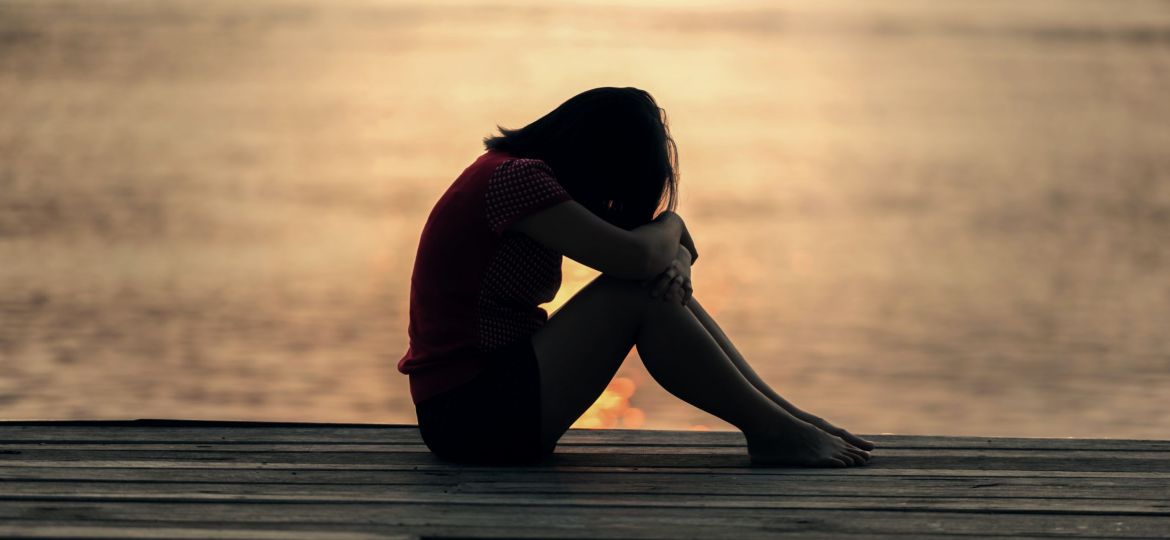 A woman with her head on her knees by the water suicide