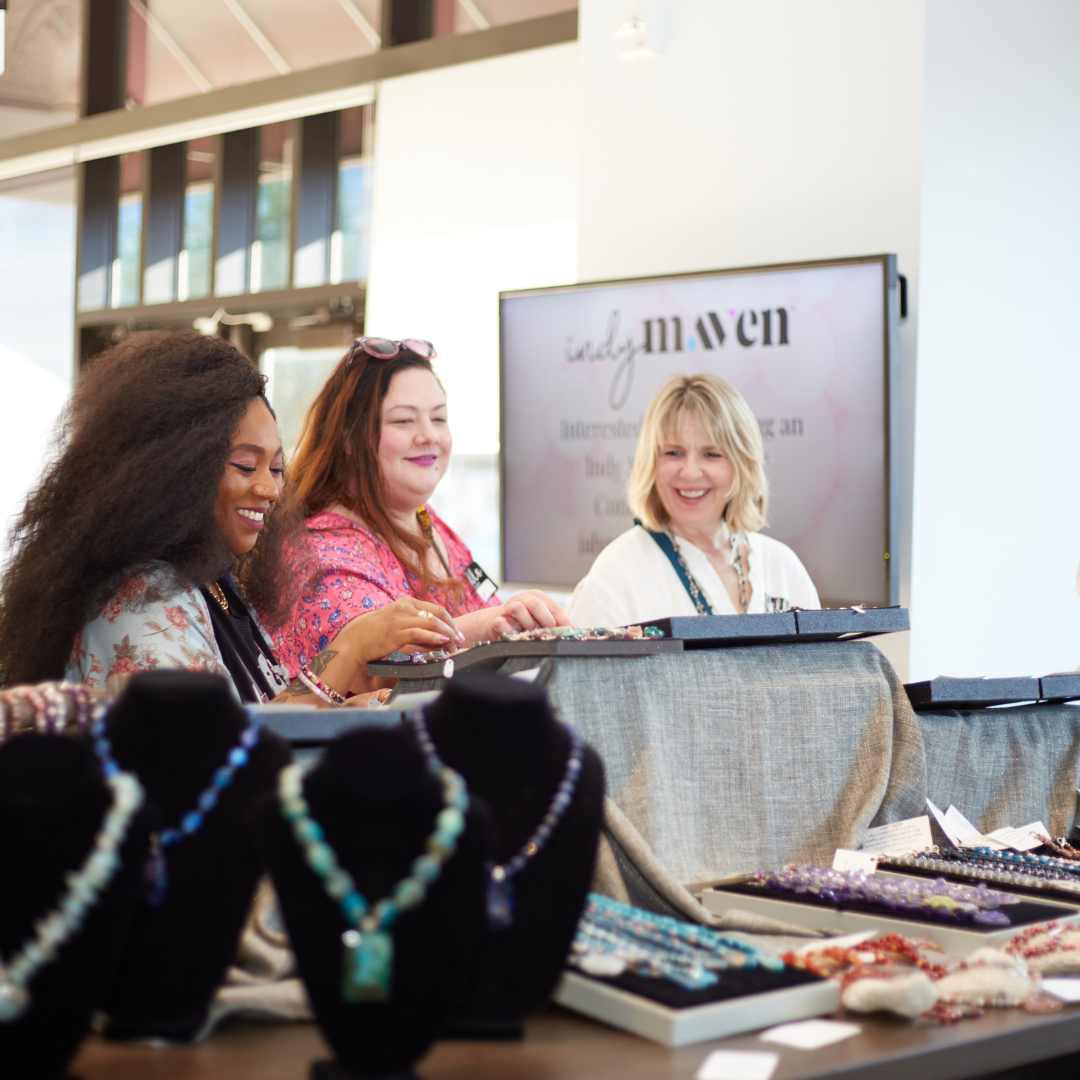 Indy Maven Meetup Women Shopping Three women shopping and admiring jewelry, a TV in the background shows the Indy Maven logo