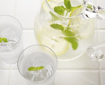 A pitcher and two glasses of water with mint in them