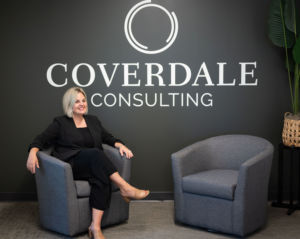 Rachael sitting in a chair with a wall behind her that reads :Coverdale consulting"