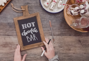 a person is writing on a chalkboard sign. it reads "hot chocolate bar"