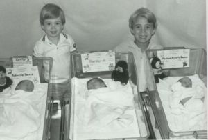 three seperate hospital baby bins with 3 babies and two small children standing behind and smiling