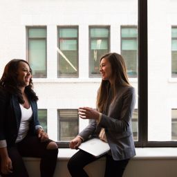 Two women sit on a windowsill laughing