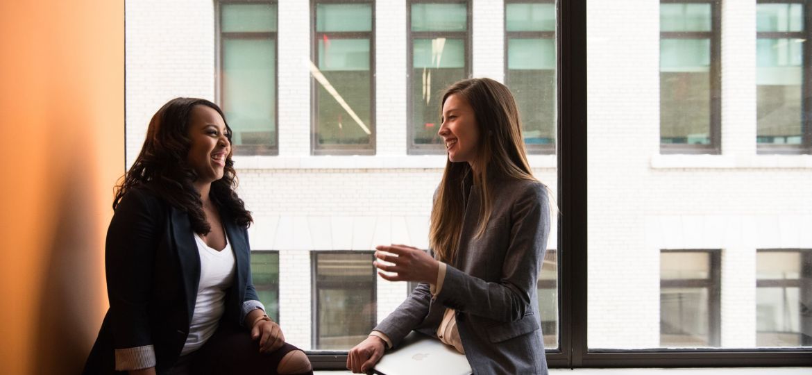 Two women sit on a windowsill laughing