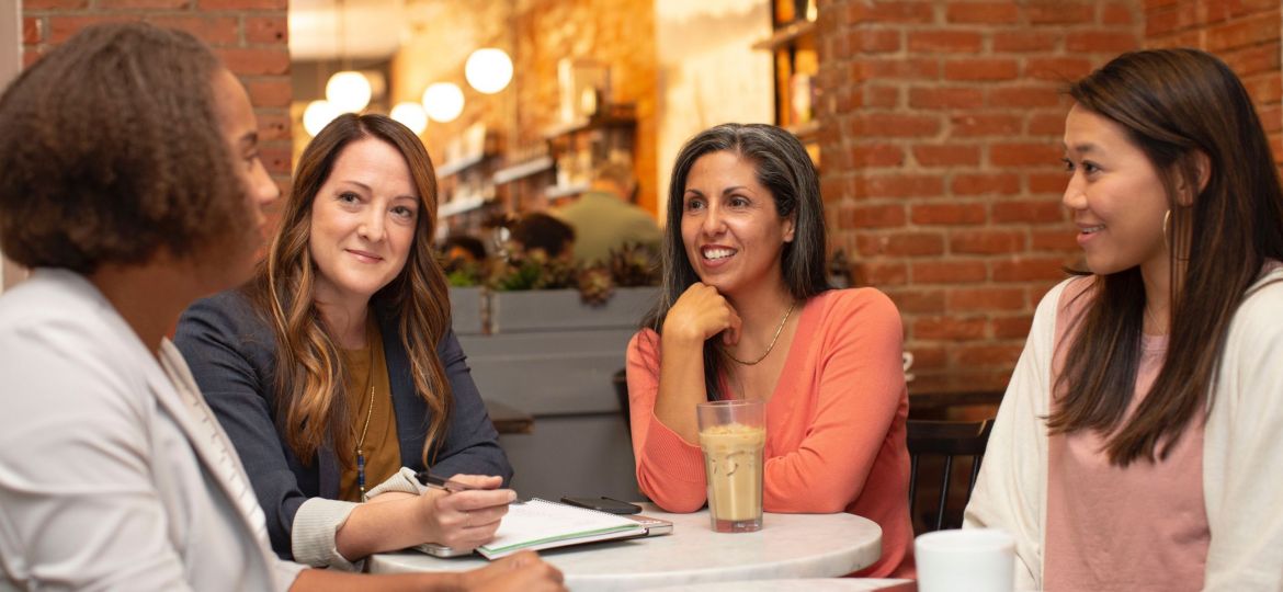 Four woman sit around a table in a coffee shop having a conversation