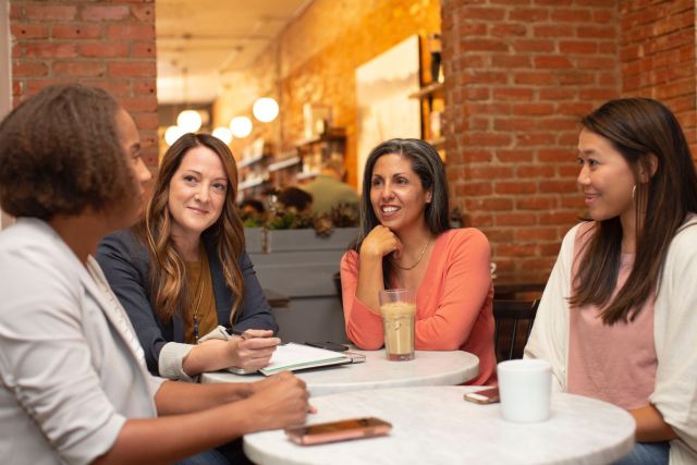 Four woman sit around a table in a coffee shop having a conversation