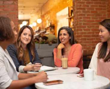 Four woman sit around a table in a coffee shop having a conversation