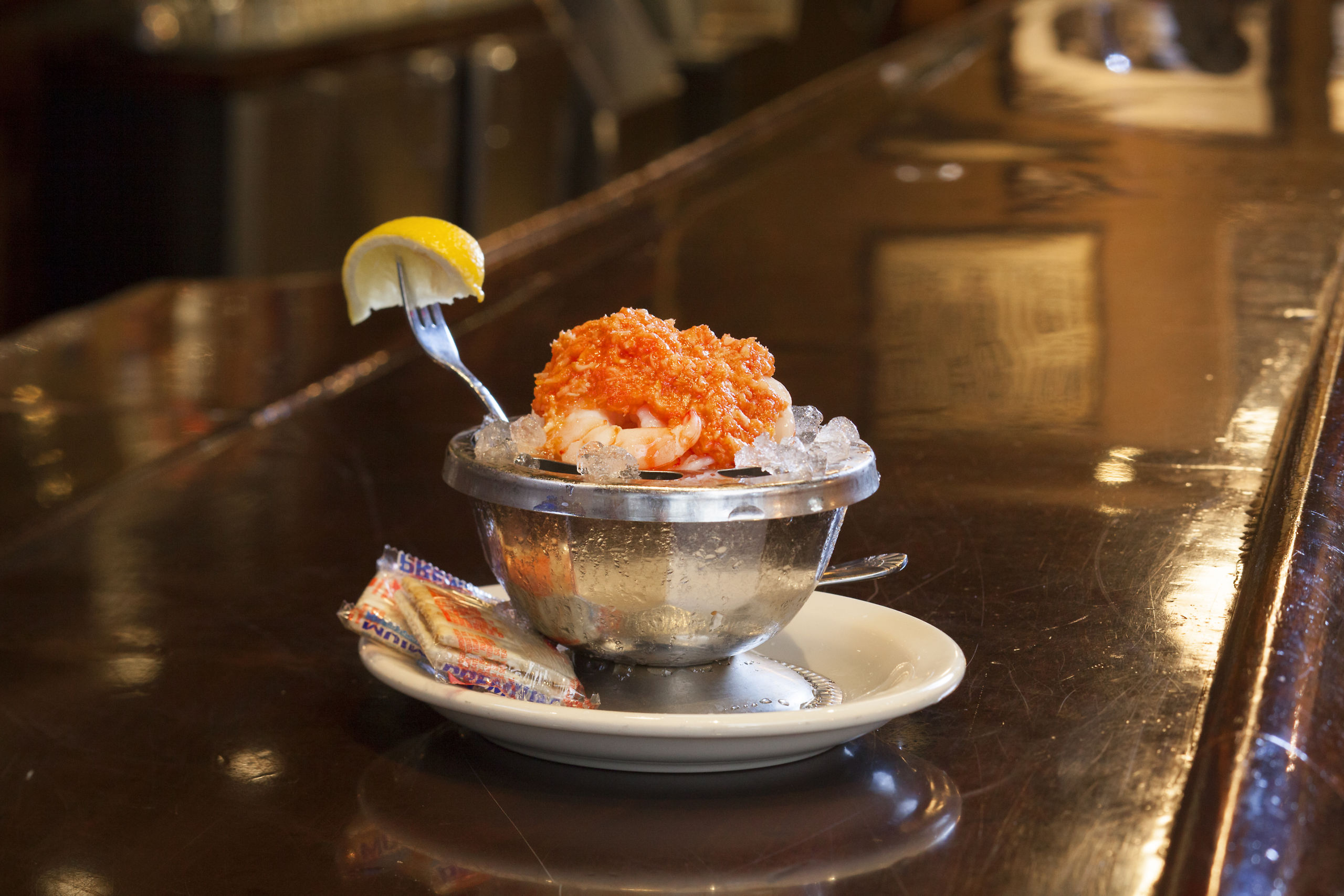 St. Emlo's shrimp cocktail served in a silver bowl with a fork stabbing a lemon