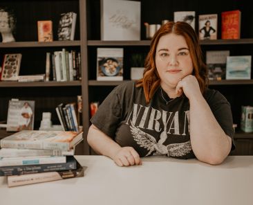 Brittney Mason sitting at a desk with a pile of books on the left