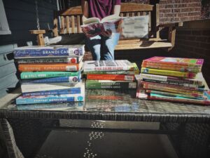 Women sitting on a porch swing surrounded by library books.