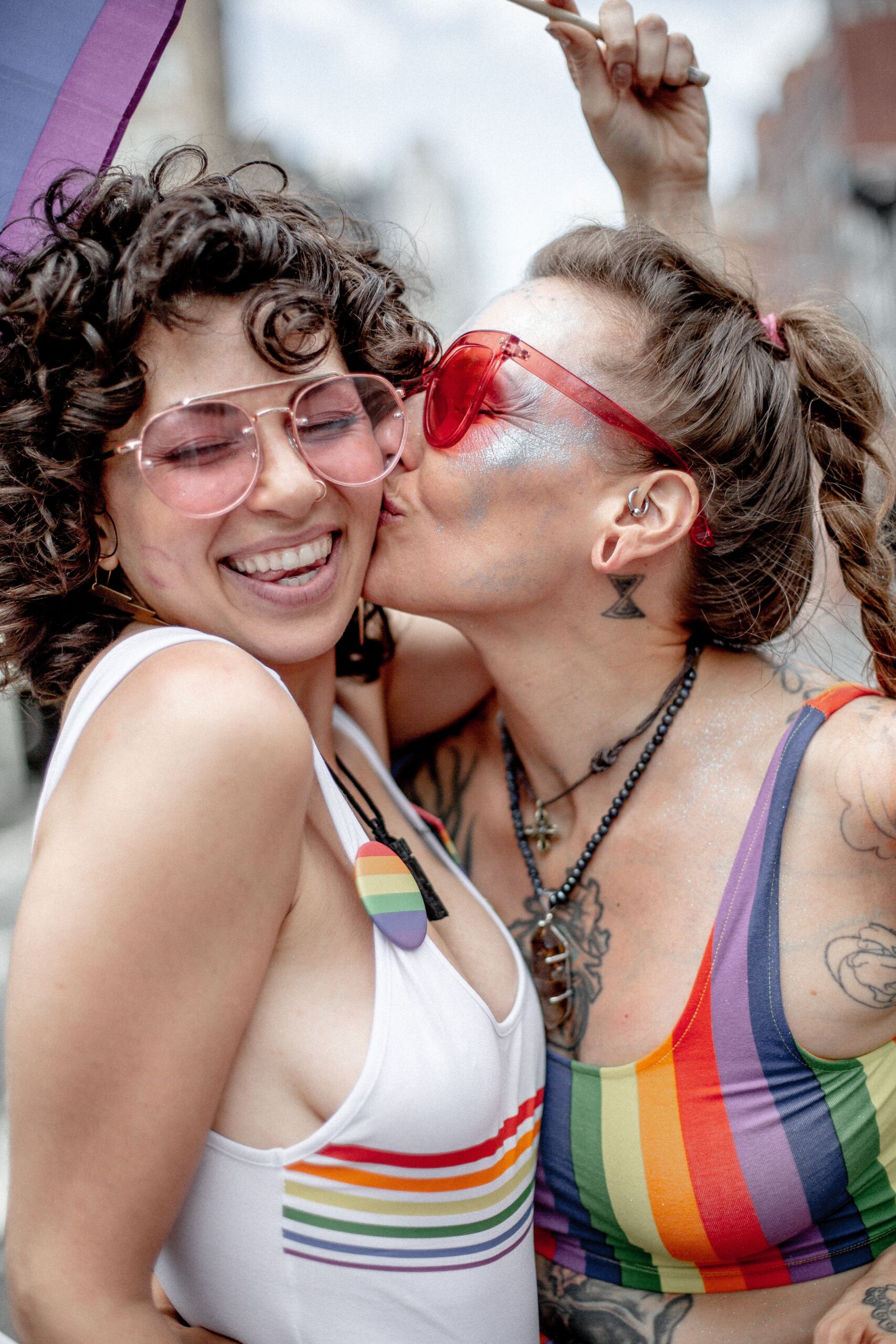 Woman in pink sunglasses kissing curly haired woman on the cheek