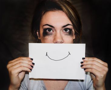 Girl with smudged mascara holding a piece of paper with a drawn smile over her mouth