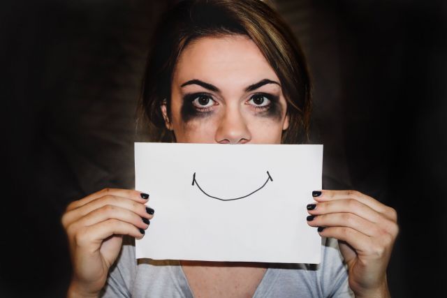Girl with smudged mascara holding a piece of paper with a drawn smile over her mouth
