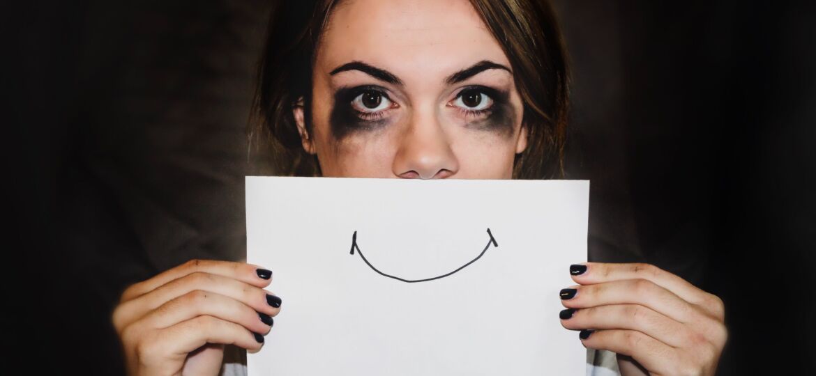 Girl with smudged mascara holding a piece of paper with a drawn smile over her mouth