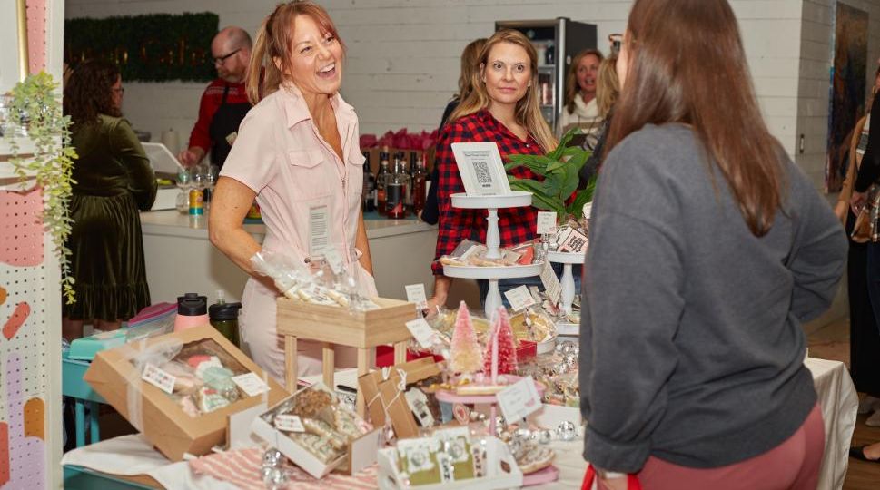 Women laughing at vendor table displaying holiday gifts