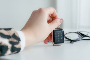 Image of a hand with an animal print sweater sleeve holding an Apple Watch next to black glasses on table.