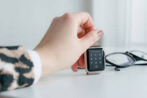 Image of a hand with an animal print sweater sleeve holding an Apple Watch next to black glasses on table.