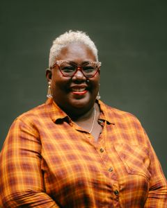 Tiffany Johnson Bass in a yellow and orange flannel button up shirt, wearing glasses.