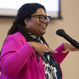 Tamara Winfrey-Harris, President of the Women's Fund of Central Indiana speaking at a microphone wearing a hot pink blazer