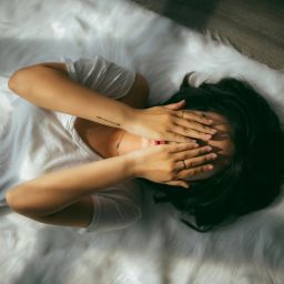 woman lying down and covering her face with her hands