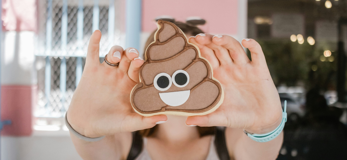 Woman hands holding a poop emoji cookie in front of her face.