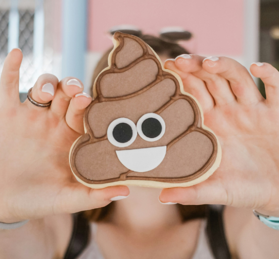 Woman hands holding a poop emoji cookie in front of her face.