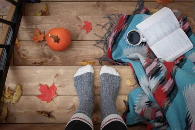 A cozy image of feet with socks on, in a fall setting, with an open book and coffee.
