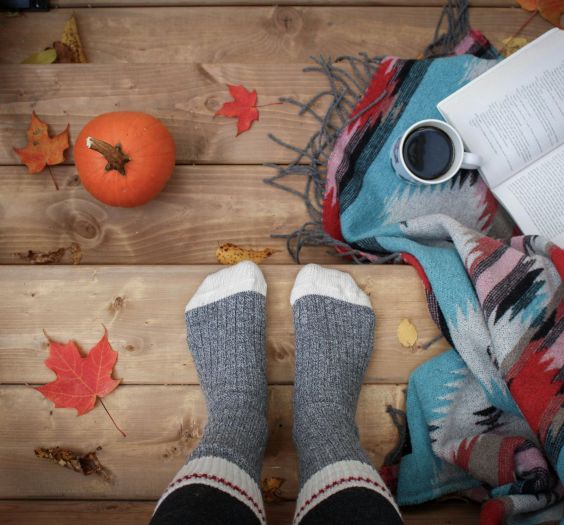 A cozy image of feet with socks on, in a fall setting, with an open book and coffee.