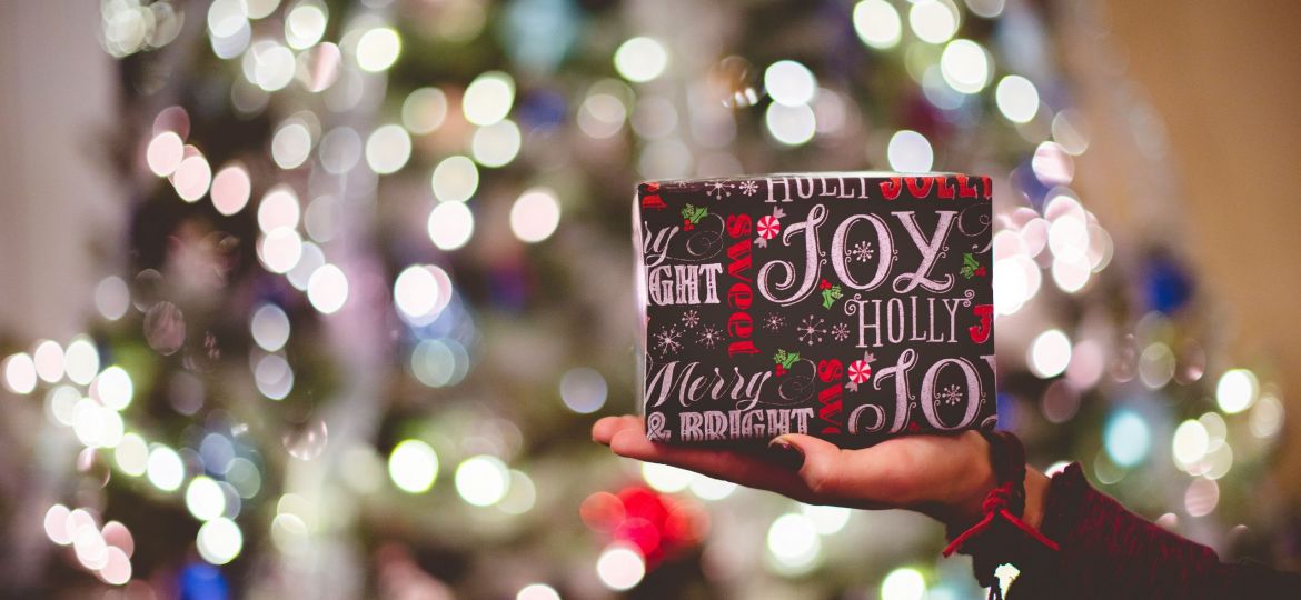 Someone holding a small present in front of a lit up tree.