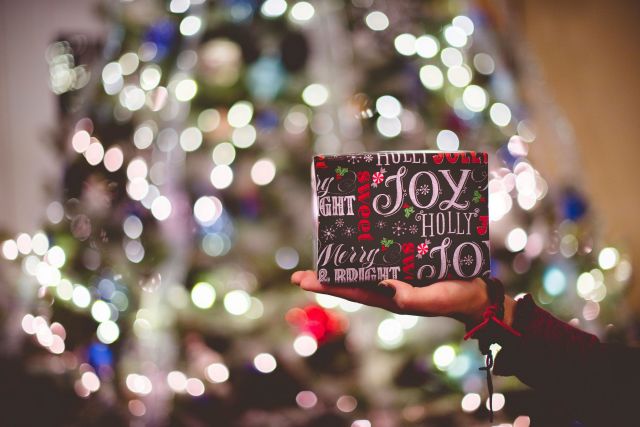 Someone holding a small present in front of a lit up tree.