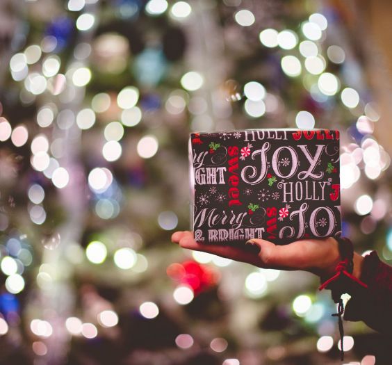 Someone holding a small present in front of a lit up tree.